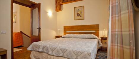 A bedroom with a wooden headboard, a patterned bedspread, a nightstand with a lamp, and a telephone.