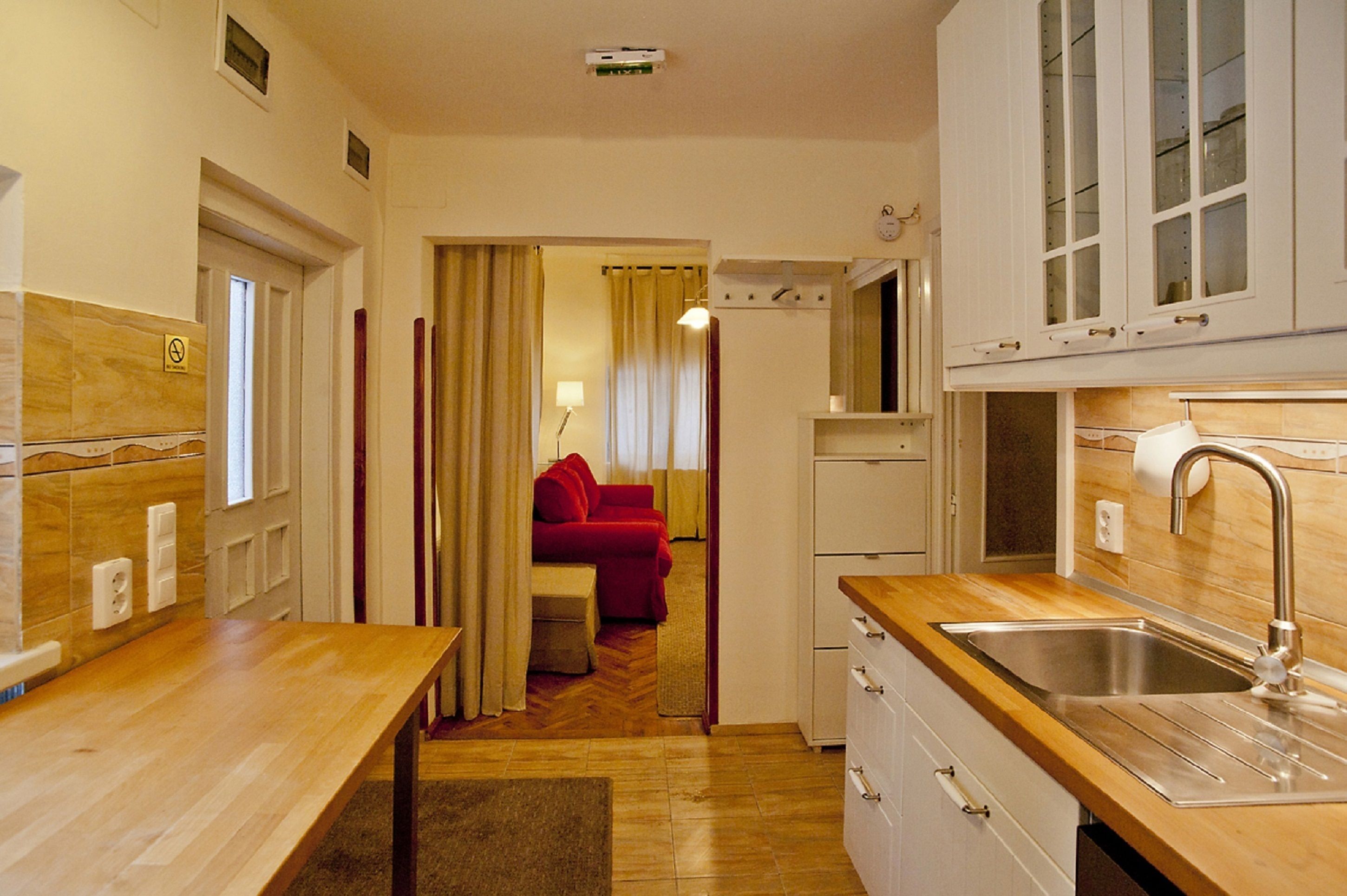 Una cocina compacta con encimera de madera, un lavamanos de acero inoxidable y un sofá rojo al fondo.