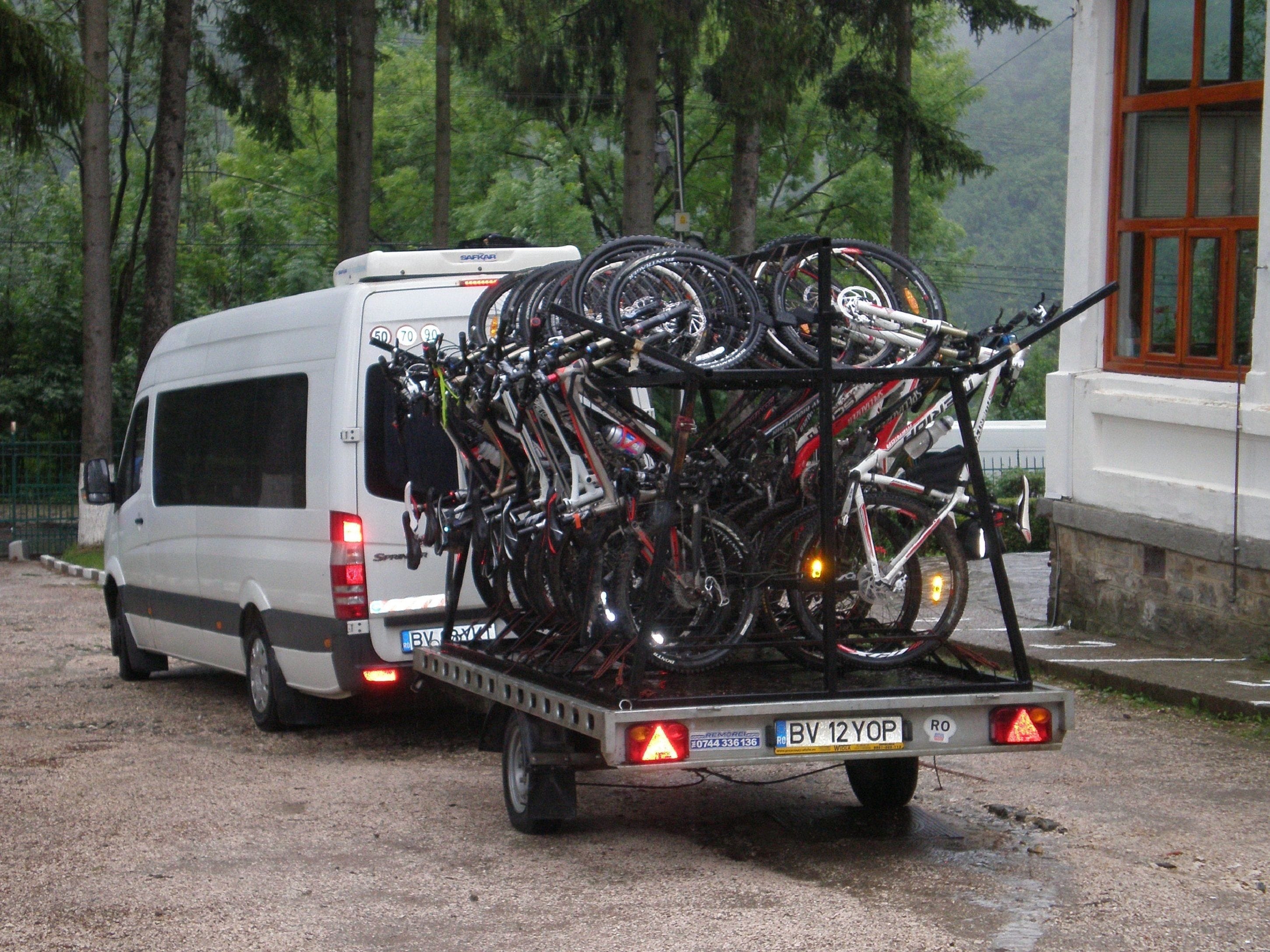 A white van with a bicycle rack loaded with multiple bicycles parked on a gravel road.