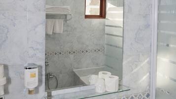 Une salle de bain avec un mur recouvert de carreaux de marbre, un lavabo en verre, un miroir avec éclairage intégré, un porte-serviettes et un espace douche.