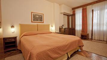 A bedroom with a large bed, wooden headboard, bedside tables, a nightstand, a framed picture on the wall, and a window with curtains.
