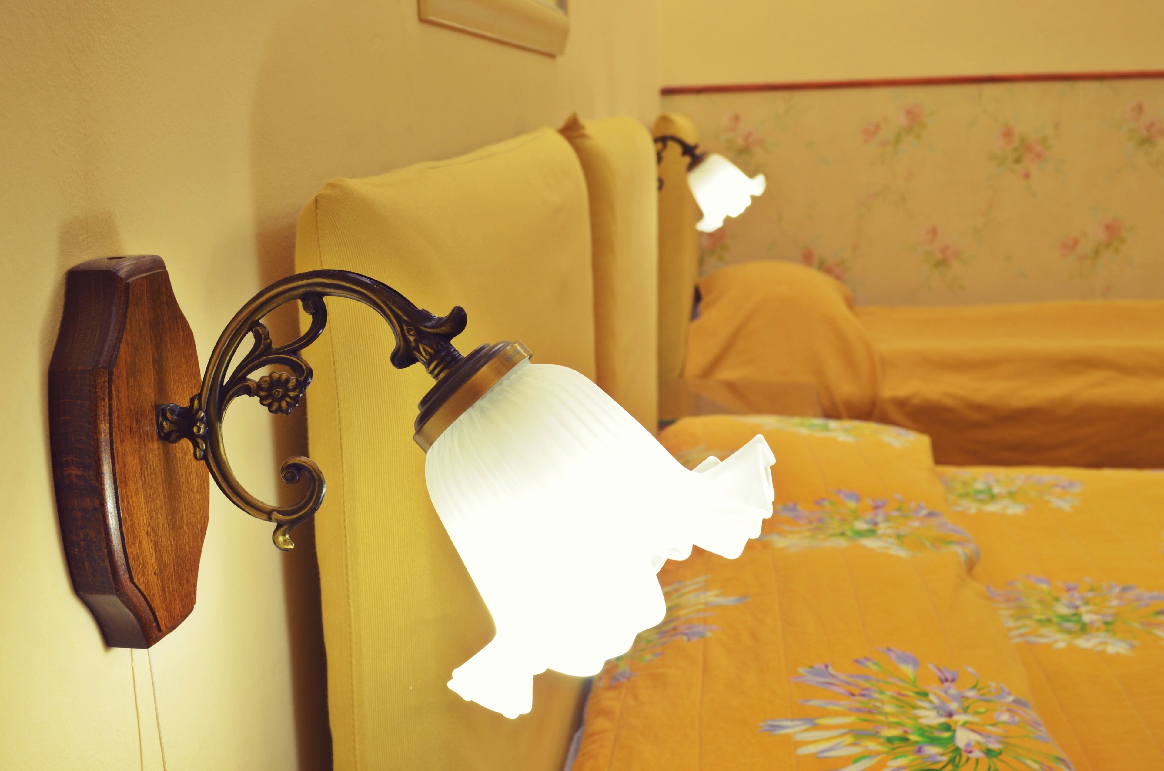 Una cama con una colcha estampada con motivos florales y una lámpara de pared.