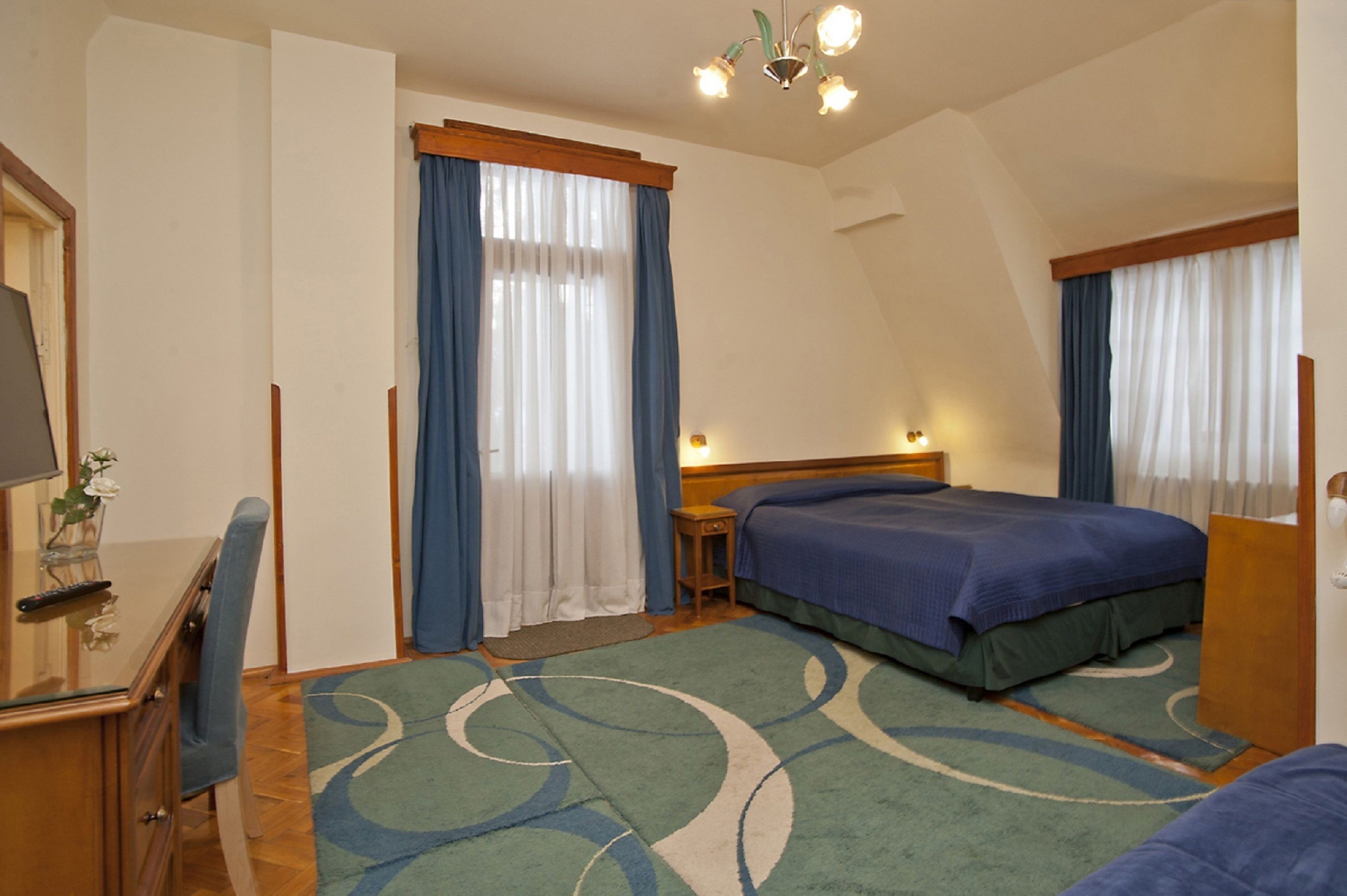 A hotel room with two beds, a desk with a chair, a small table, and a nightstand.