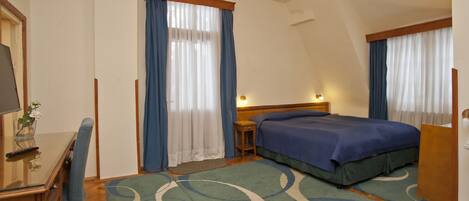 Habitación de hotel con dos camas, un escritorio con silla, una mesita pequeña y una mesita de noche.