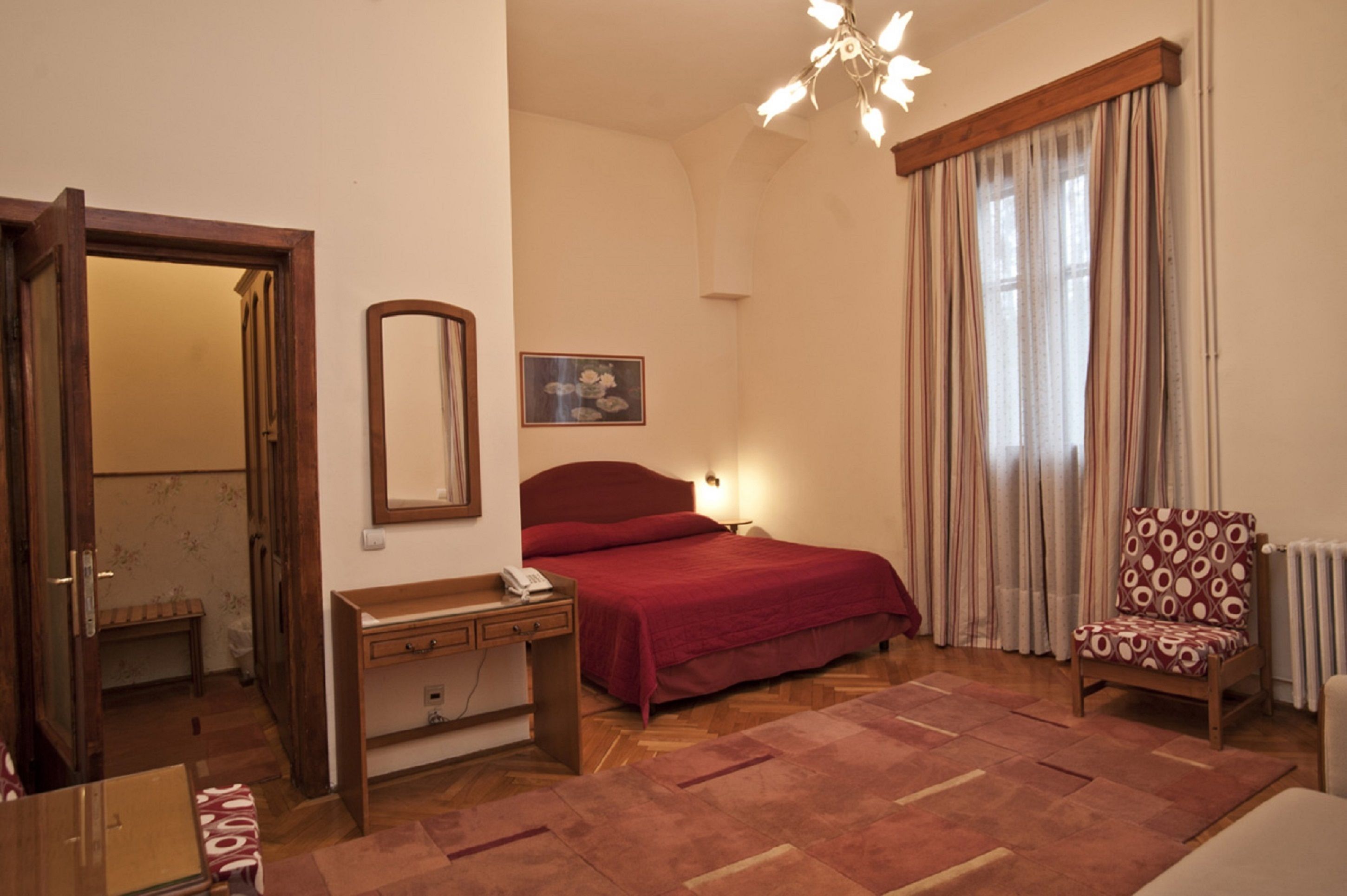 A bedroom with a bed, bedside table, chair, and a mirror.