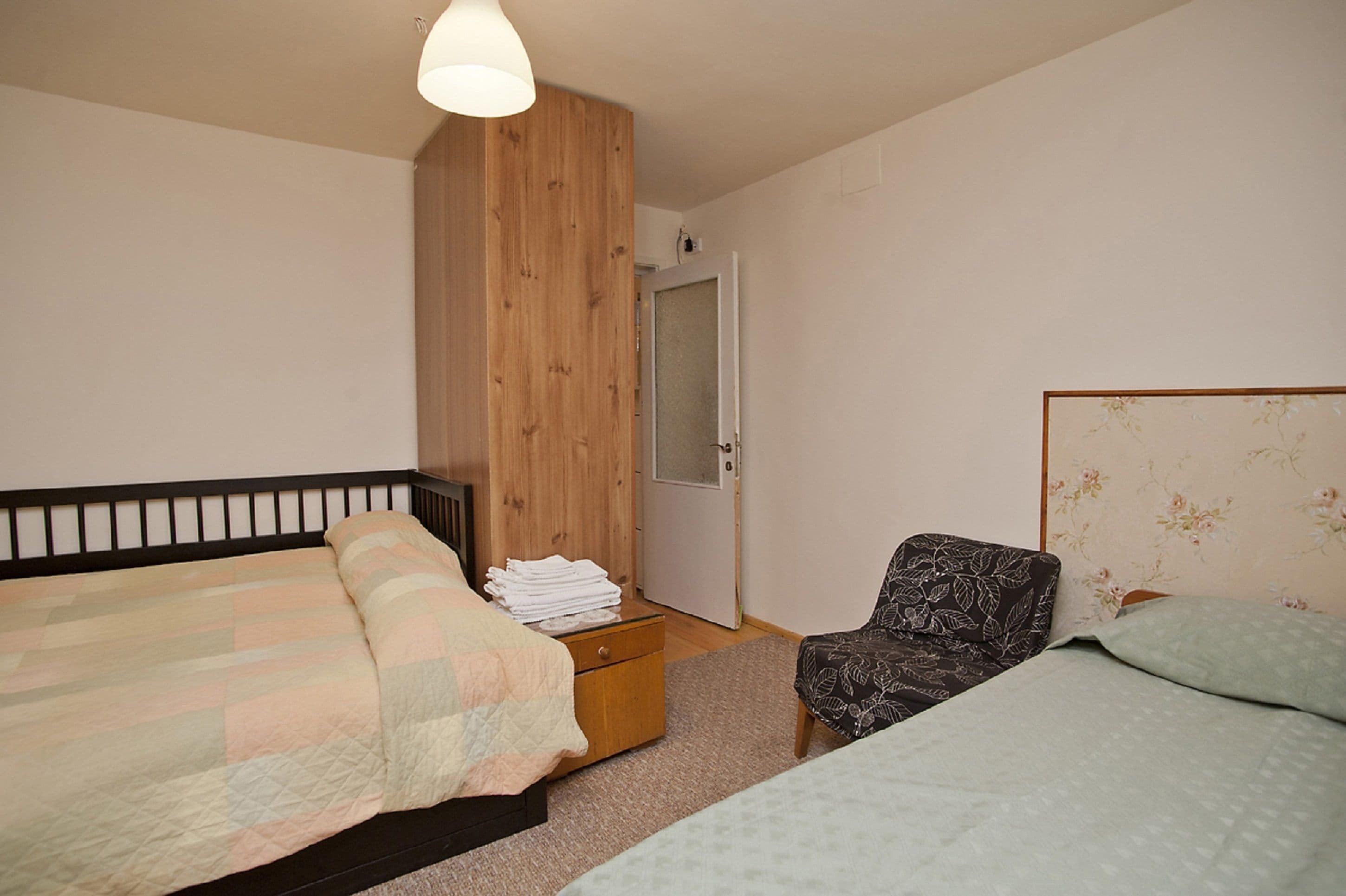 Un dormitorio con dos camas, un armario de madera, una silla y una mesita con toallas dobladas.
