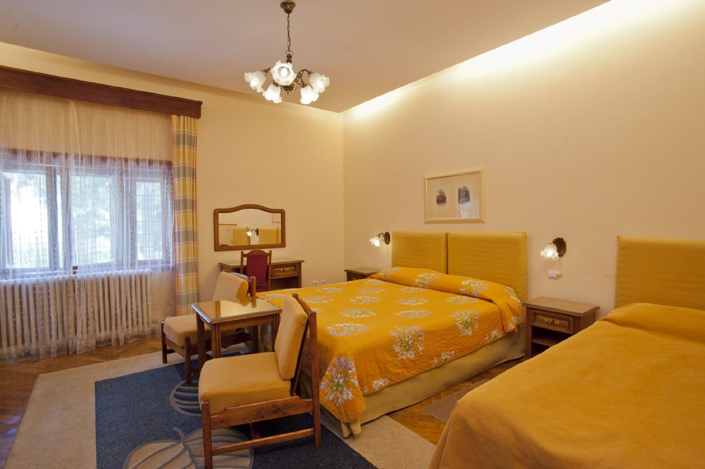 A hotel room with a bed, a desk, a chair, a small table, and a lamp.