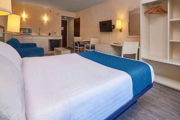 A hotel room with a large bed, a desk with a chair, a television, and a wardrobe.