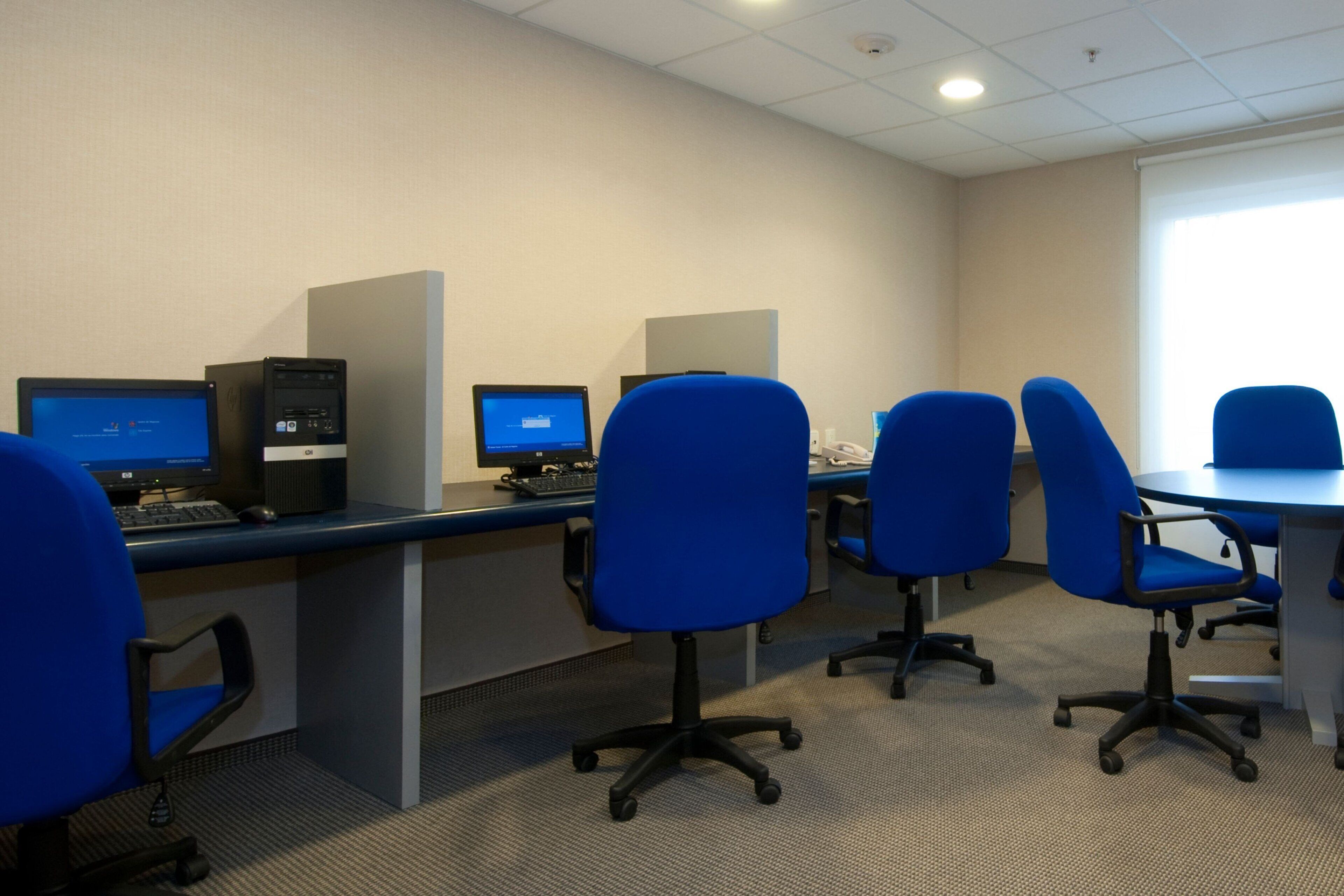 A modern office space with multiple workstations, blue office chairs, and a carpeted floor.