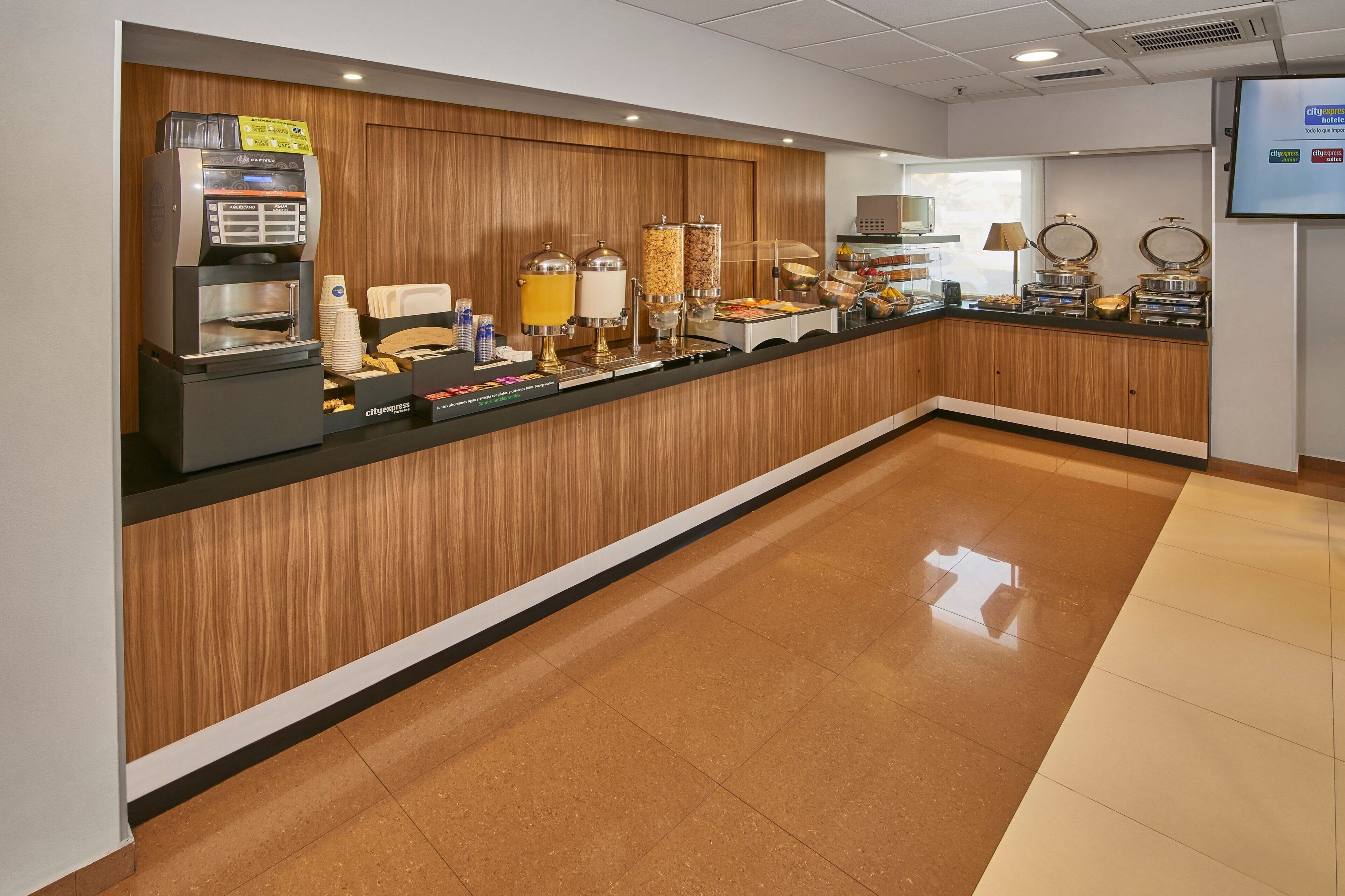 Uma área de recepção de hotel com uma máquina de café, distribuidores de comida e uma tela de TV.