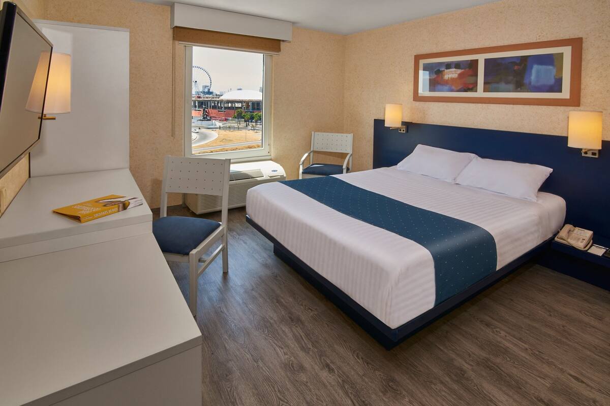 A hotel room with a bed, desk, chair, and a window with a view of a cityscape.