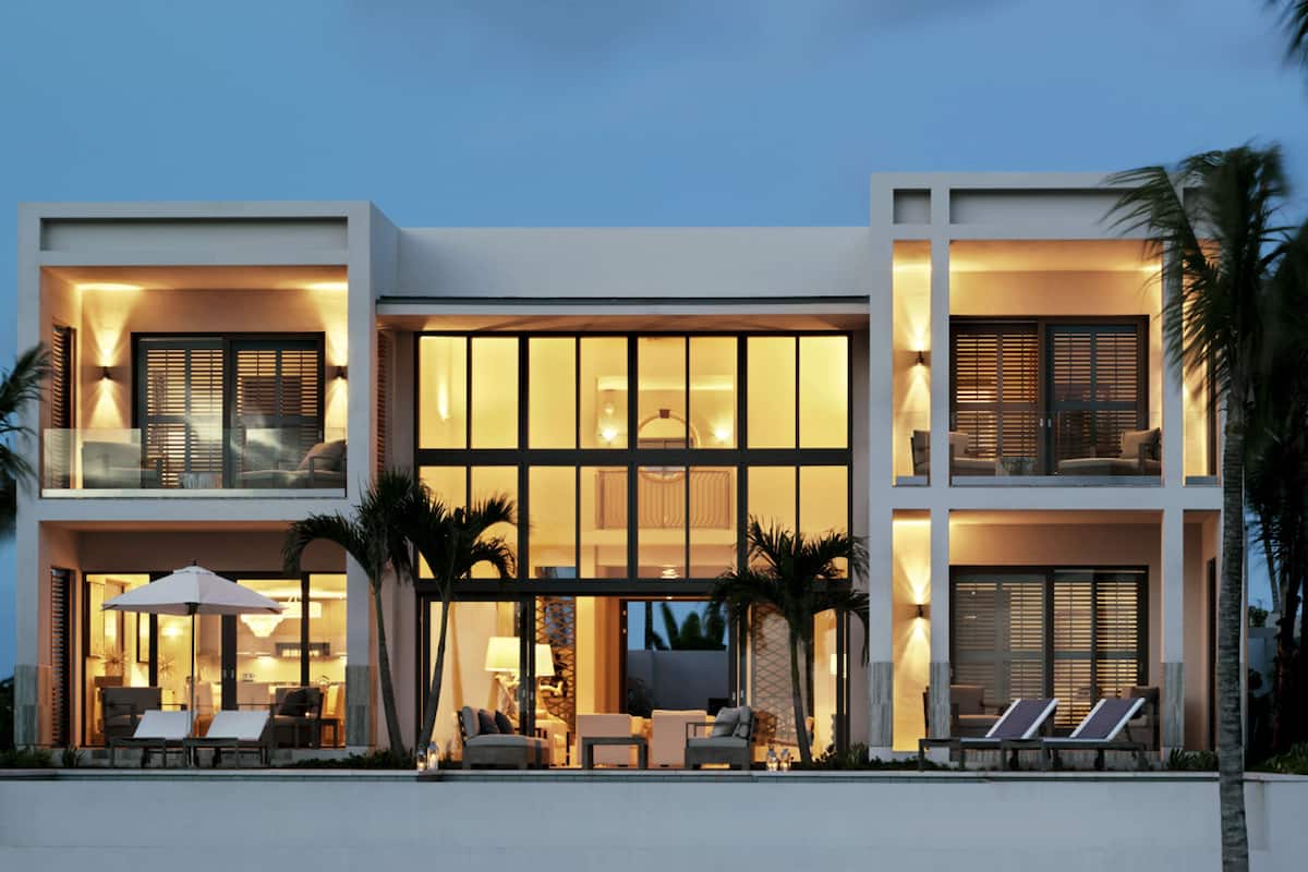Een modern huis met twee verdiepingen, een balkon, grote ramen en buitenmeubels.