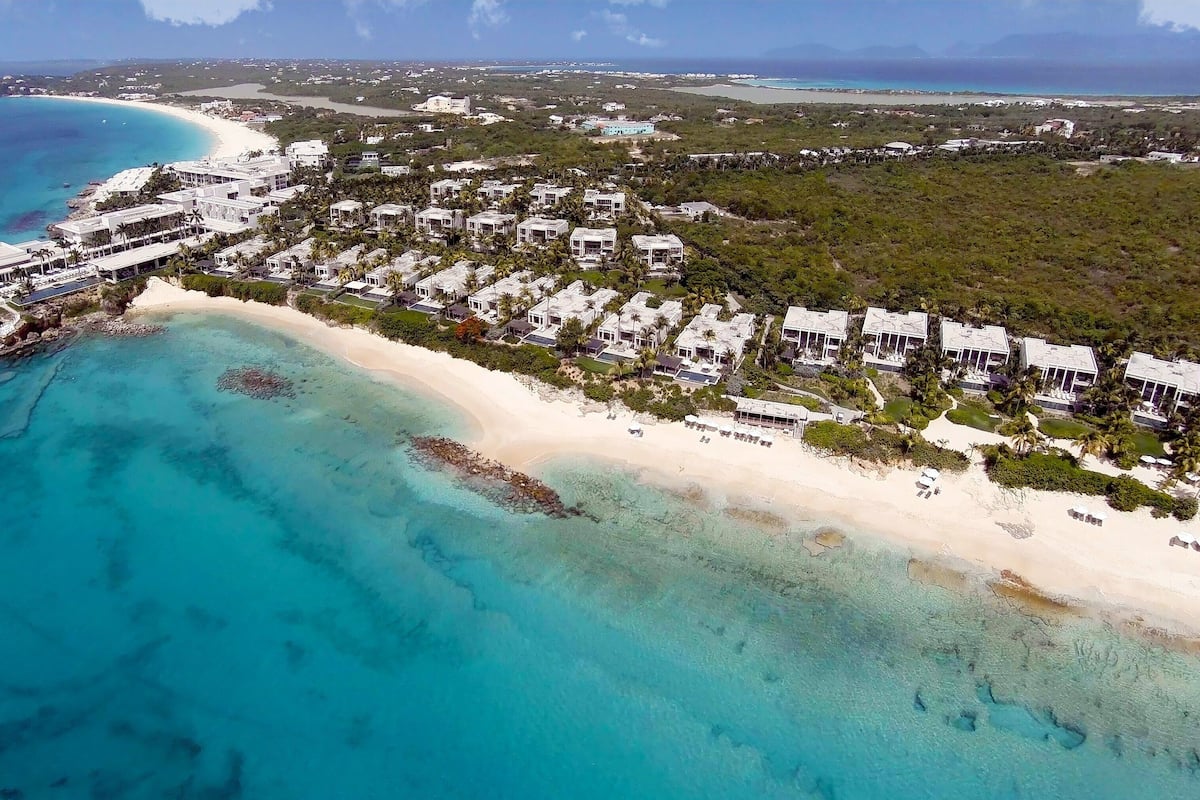 Luchtbeeld van een kustresort met villa's aan het strand, helder turquoise water en een zandstrand.