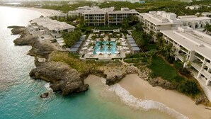 An aerial view of a resort with a central swimming pool, beachfront, and multiple buildings. - Four Seasons Resort and Residences Anguilla (West End Village)