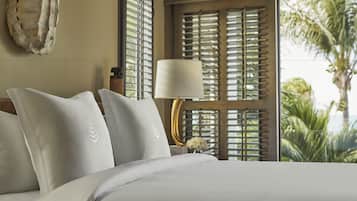 A neatly made bed with white linens and a decorative pillow. A bedside table with a lamp and a vase of flowers is visible.
