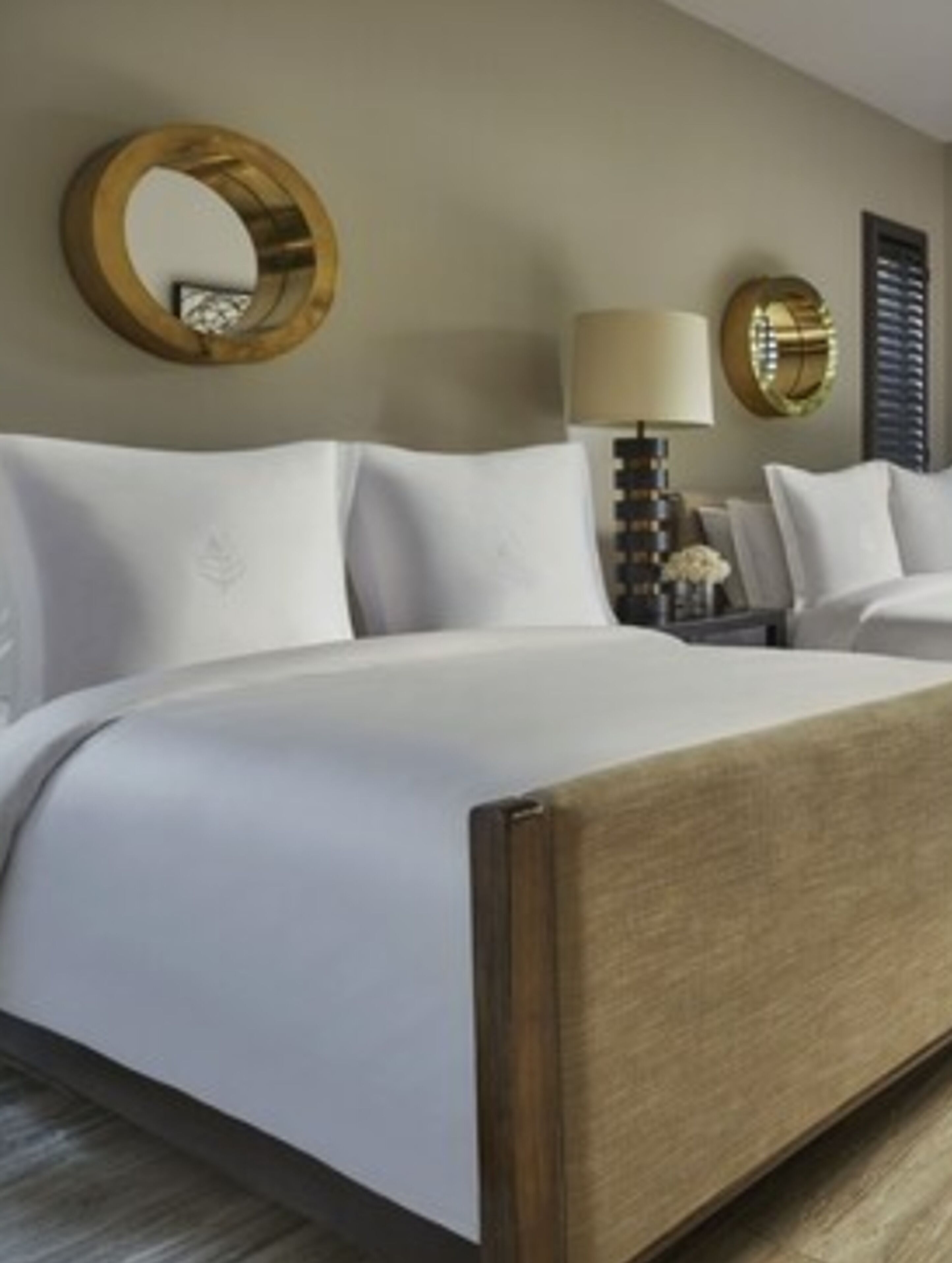 Quarto de hotel com uma cama grande, mesa de cabeceira com abajur e um espelho redondo na parede.