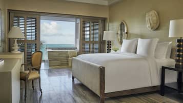 A hotel room with a large bed, a desk, a chair, and a view of the ocean through the window.
