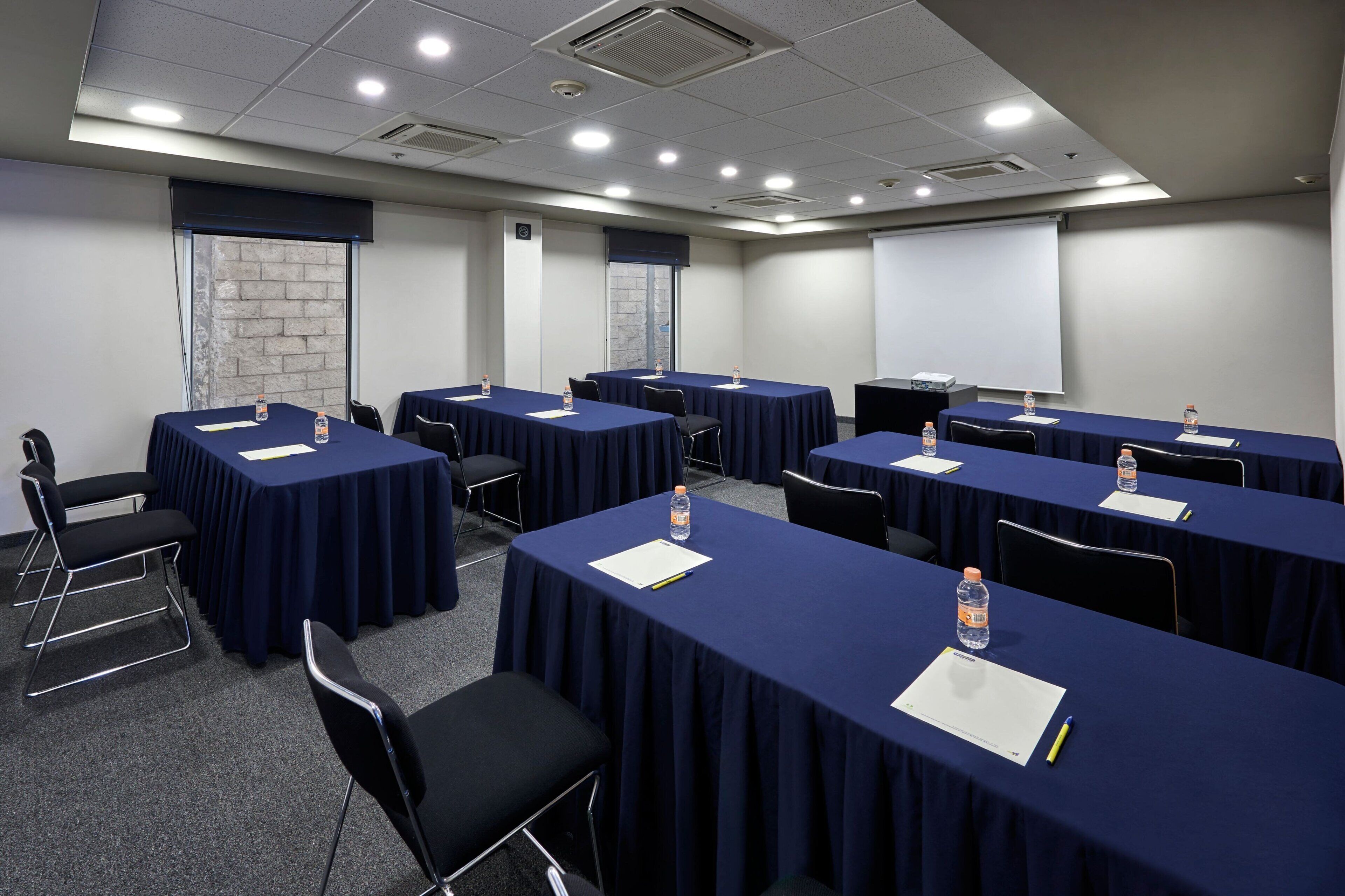 Une salle de conférence équipée de plusieurs tables, de chaises et d’un écran de projection.