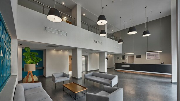 A spacious lobby with grey sofas, a wooden coffee table, and pendant lighting. - City Express by Marriott Tijuana Río (Tijuana)