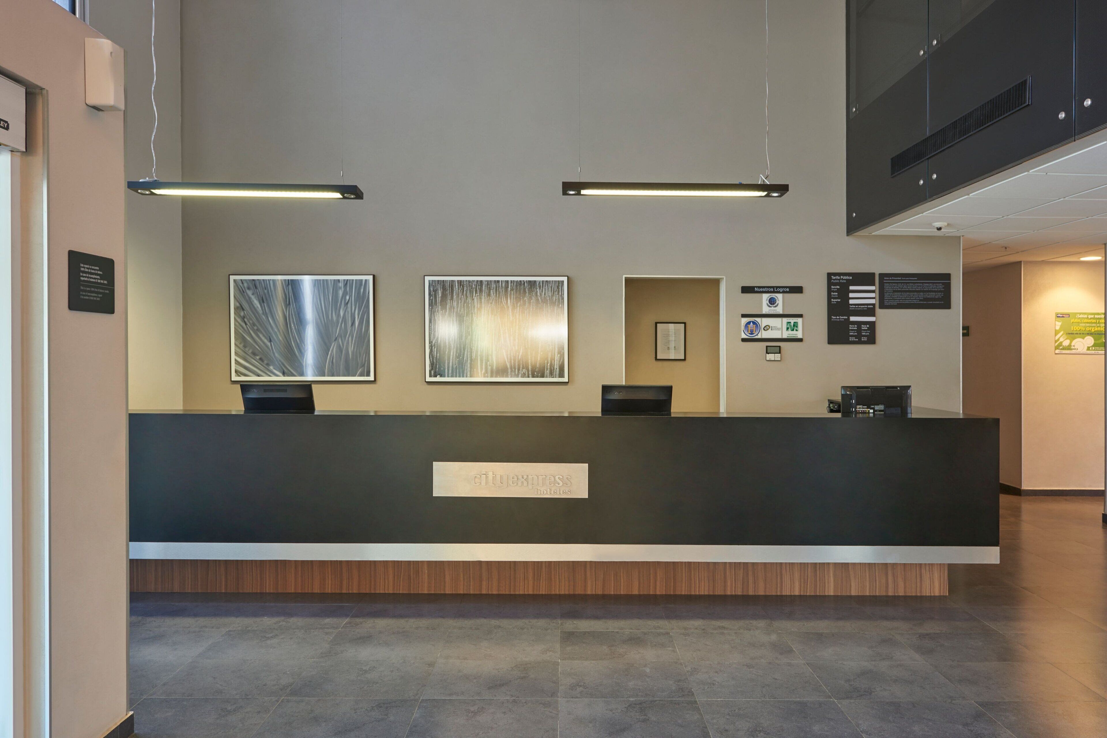 A reception desk with a sign reading "cityexpress hotels," two framed artworks on the wall, and a digital information board.