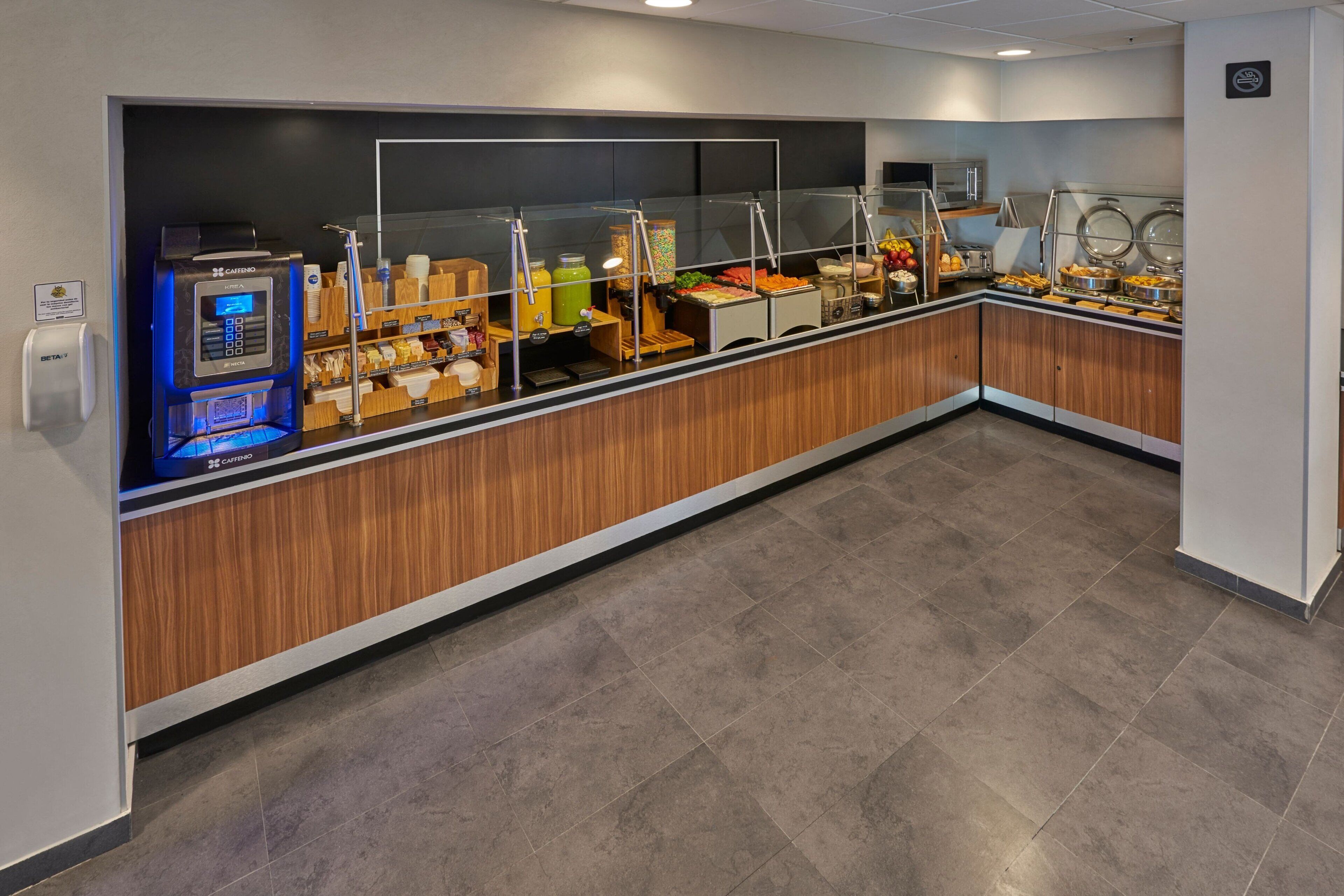 Espai de desguàs per esmorzar, amb una màquina de comandes digital, diferents aliments i una màquina de cafè.