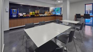 Un comedor moderno con mostrador de buffet, mesas blancas y sillas negras.