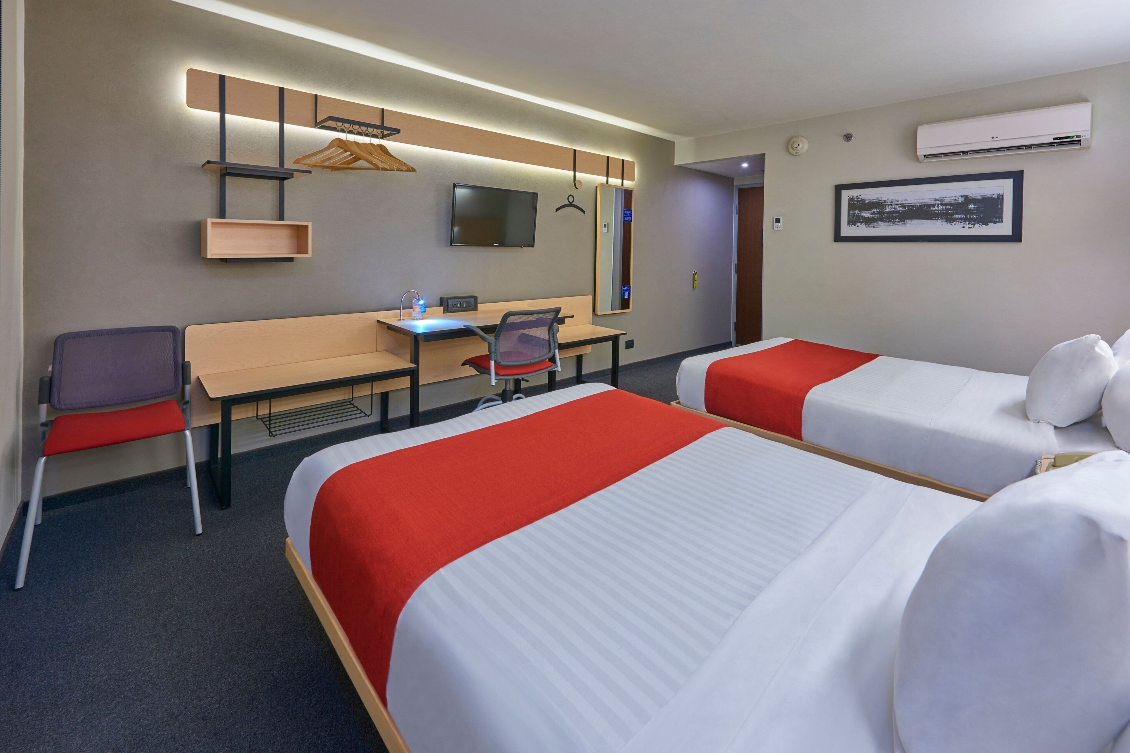 Una habitación de hotel con dos camas, un escritorio, una silla, un televisor y un espejo.