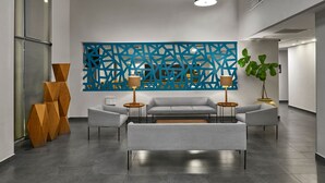 A modern lobby with a grey sectional sofa, two side chairs, a blue geometric wall art, and a potted plant. - City Express by Marriott Tijuana Río (Tijuana)