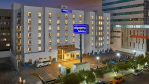 A CityExpress Hotel with a modern design, featuring a central entrance, multiple floors, and a parking area with several cars. - City Express by Marriott Tijuana Río (Tijuana)