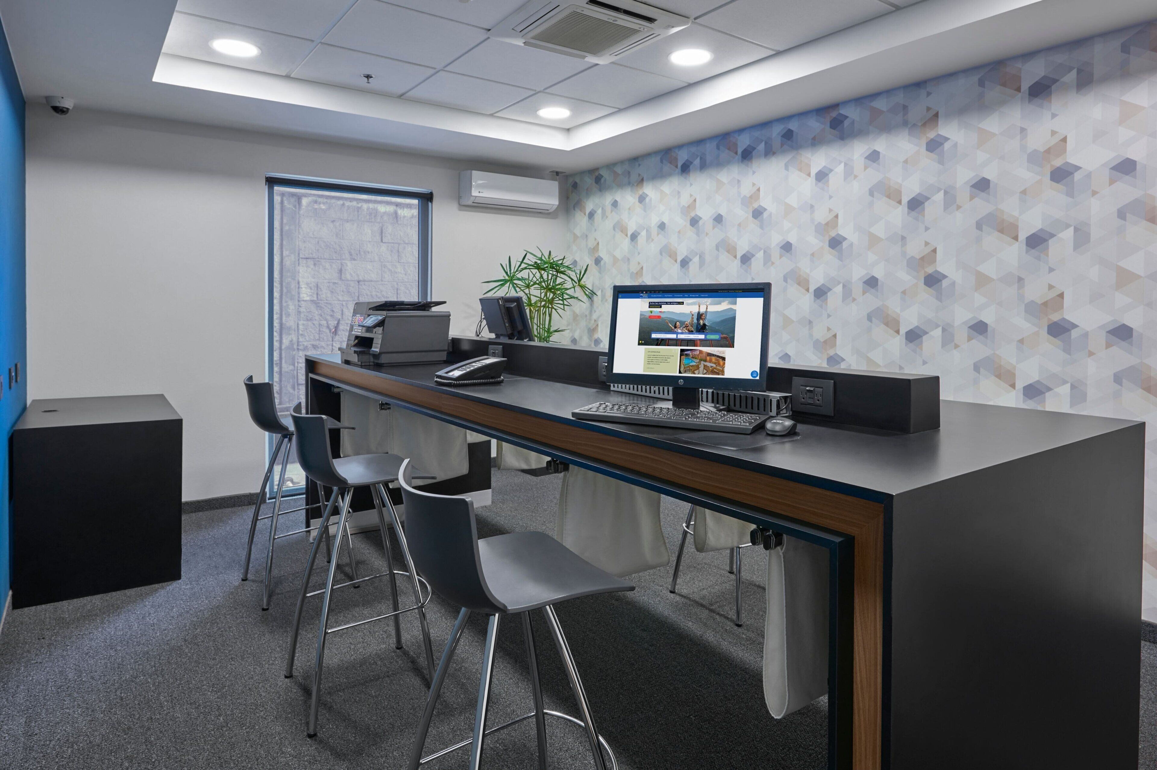 Un espacio de oficina moderno con una barra larga, dos taburetes y una computadora de escritorio con un monitor grande.