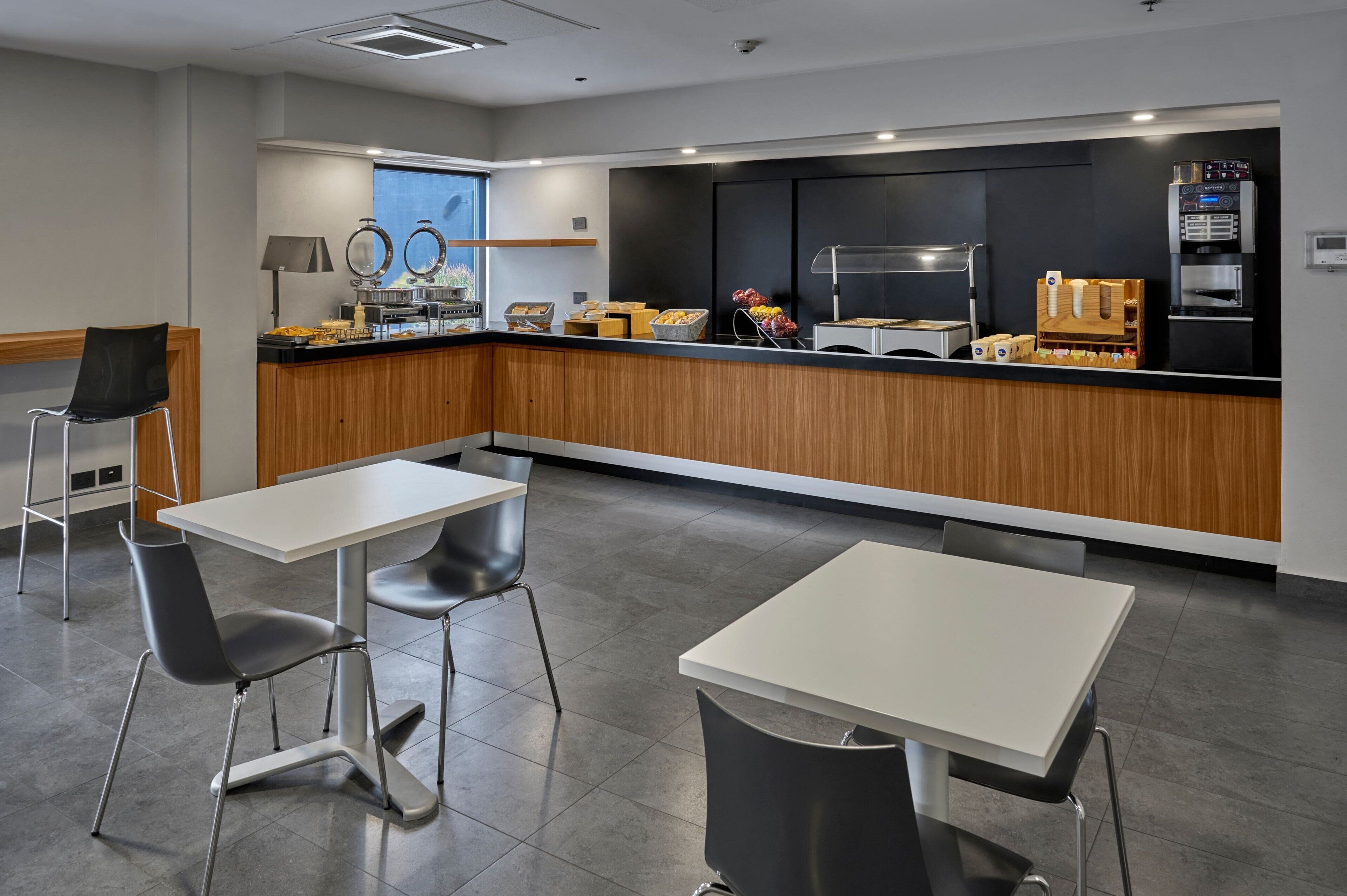 A modern kitchen area with a counter, coffee machine, and seating area with tables and chairs.