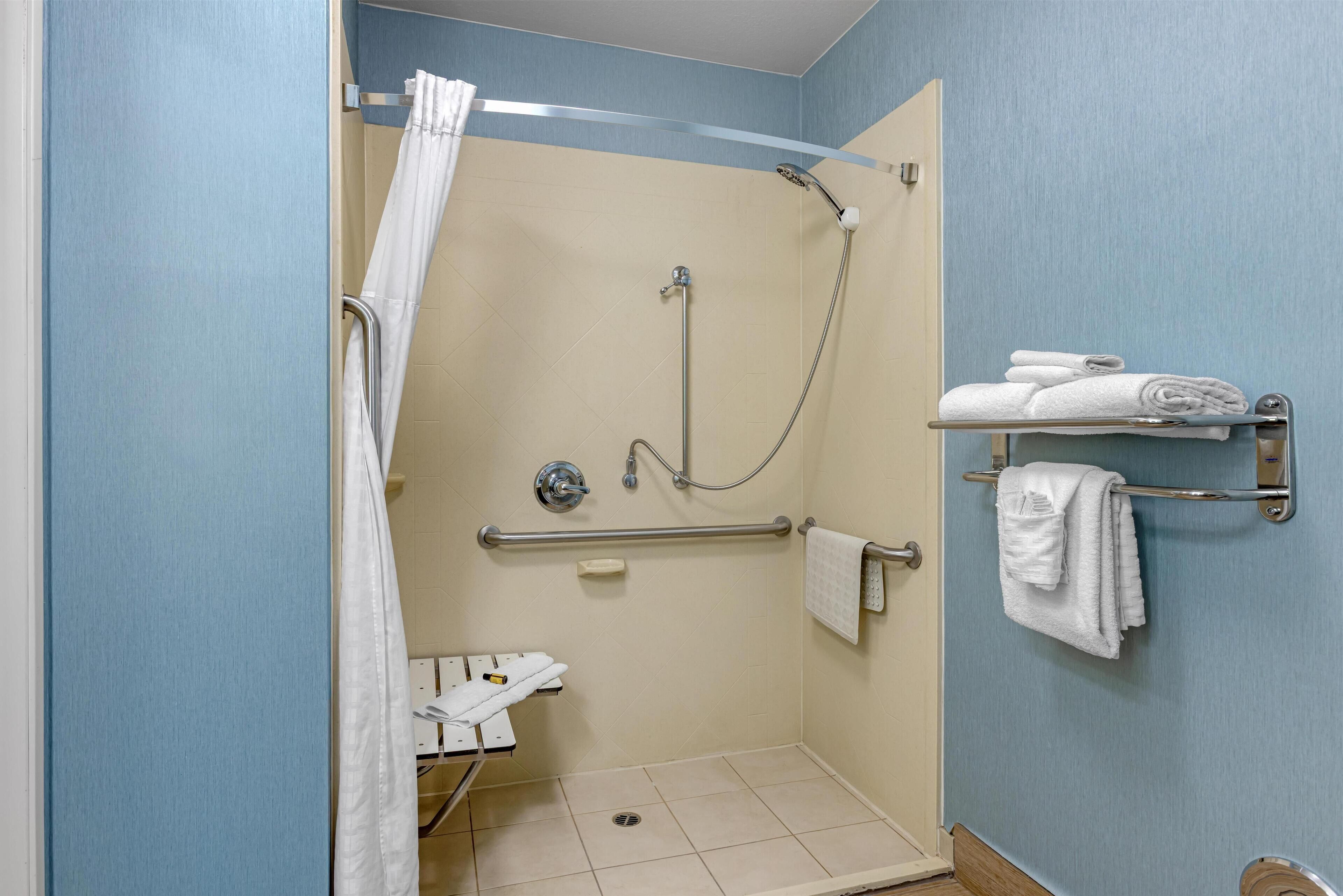A wheelchair-accessible shower with a grab bar, a white towel rack, and a shower curtain.