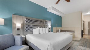 Una habitación de hotel moderna con una cama grande, un sofá, un baño con bañera y un ventilador de techo.