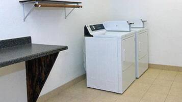 Uma área de lavanderia com máquina de lavar e secadora, uma bancada e um porta-toalhas.