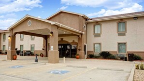 Entrada de hotel con área de espera cubierta, estacionamiento accesible para discapacitados y cielo despejado.
