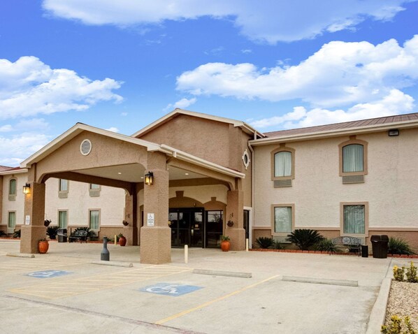 A hotel entrance with a covered waiting area, handicap accessible parking, and a clear sky.