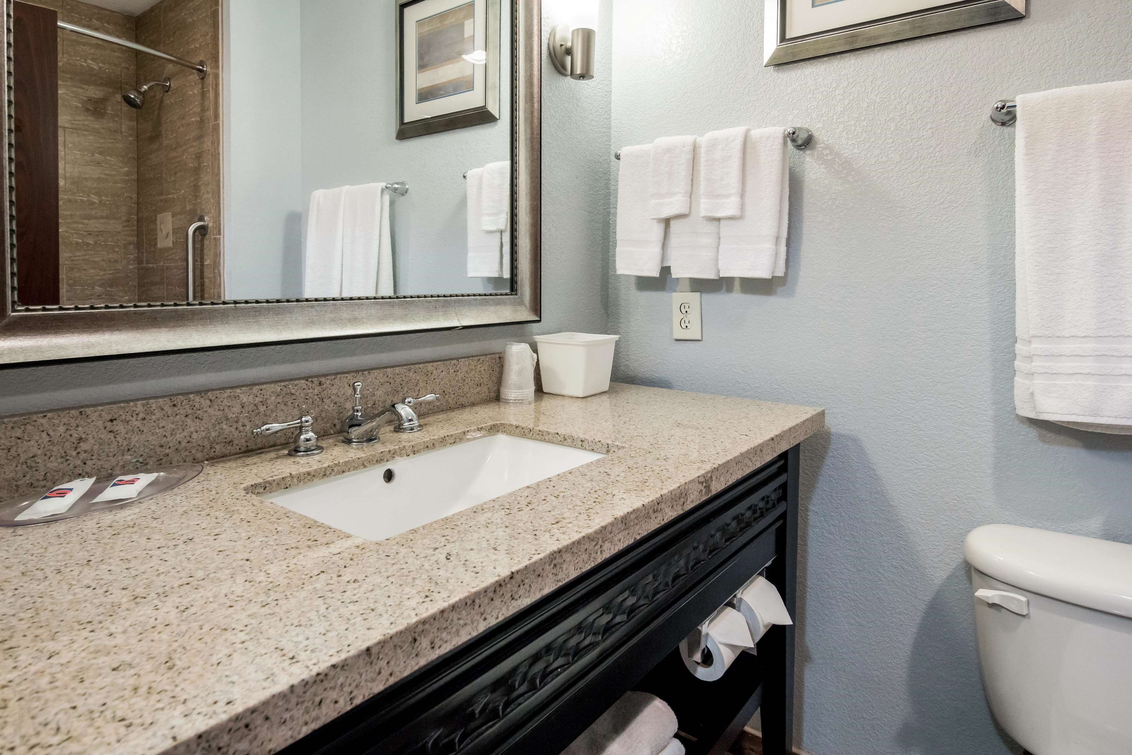 A bathroom with a granite countertop sink, a mirror, a toilet, and two towels hanging on the wall.