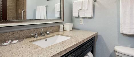 A bathroom with a granite countertop sink, a mirror, a toilet, and two towels hanging on the wall.