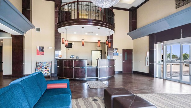 A spacious lobby with a reception desk, a blue sofa, a brown ottoman, and a patterned rug. - Baymont by Wyndham Mineral Wells (Mineral Wells)
