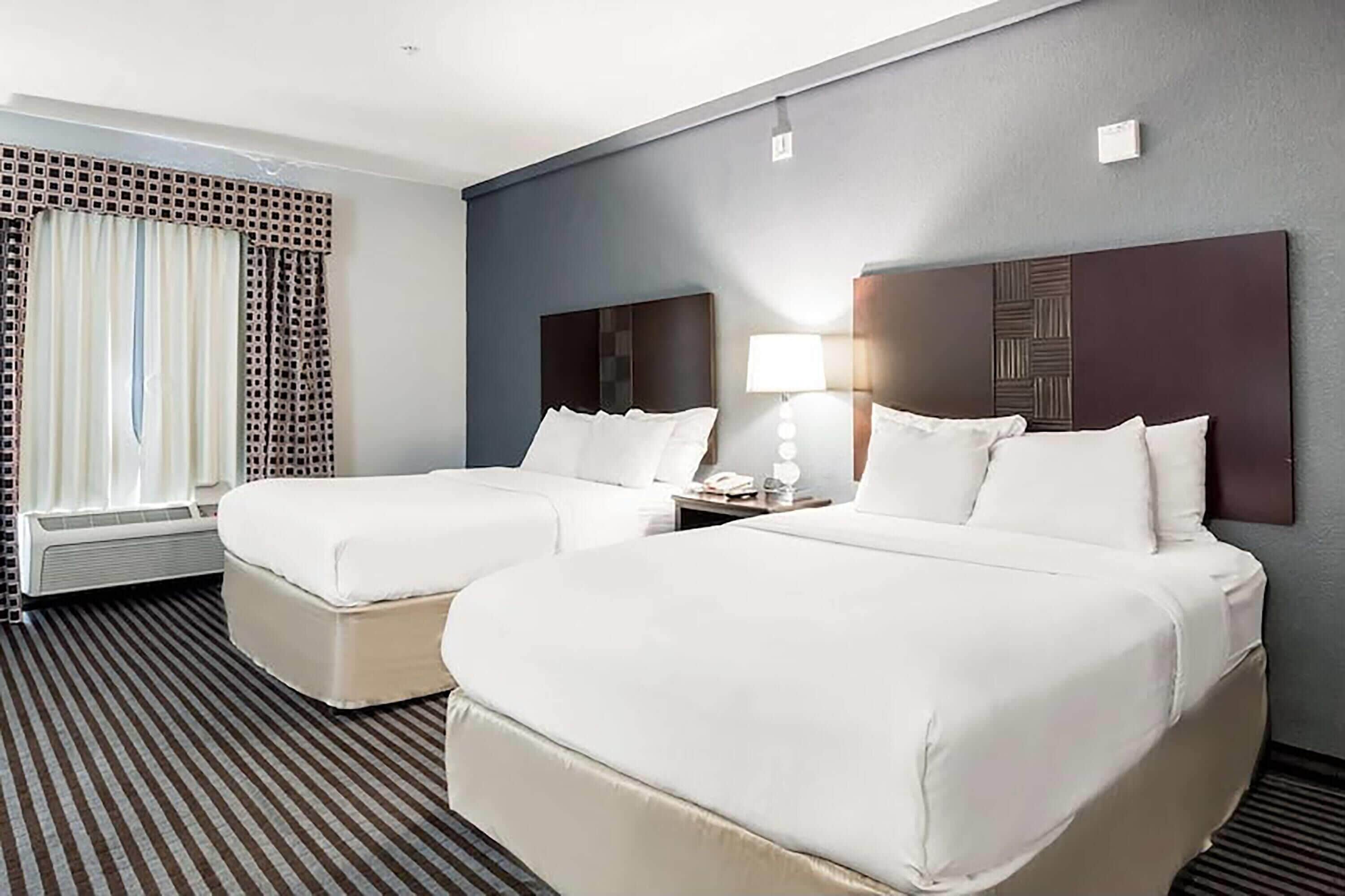 Una habitación de hotel con dos camas, una ventana con cortinas, una mesita de noche con lámpara y un radiador.
