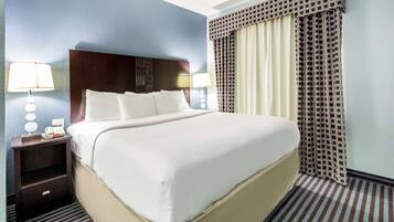 A hotel room with a large bed, a nightstand with a lamp, and a window with patterned curtains.