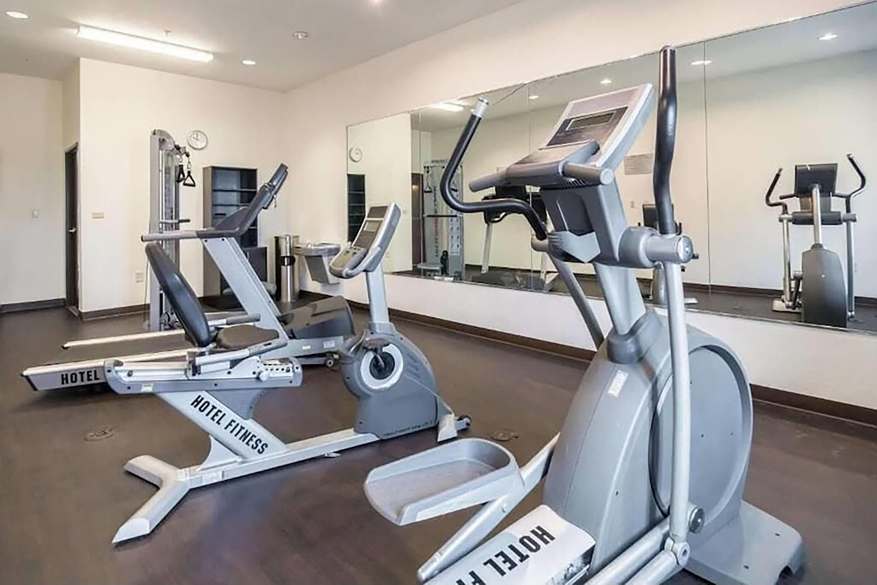 A hotel fitness center with cardio machines, a mirrored wall, and a clock.