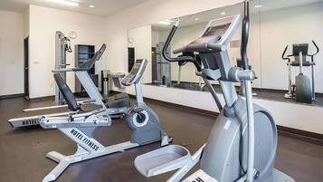 A hotel fitness center with cardio machines, a mirrored wall, and a clock.