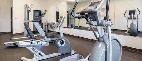 A hotel fitness center with cardio machines, a mirrored wall, and a clock.