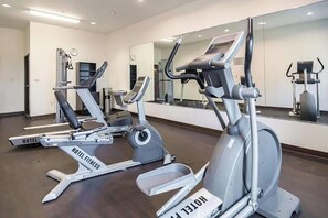 Et hotel fitnessrum med løbebånd, spejl og et ur.