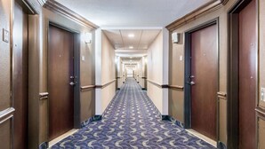 A hotel corridor with a patterned carpet, wooden doors, and a long hallway leading to a bright end. - Baymont by Wyndham Mineral Wells (Mineral Wells)