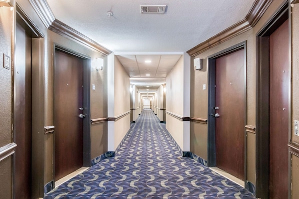 A hotel corridor with a patterned carpet, wooden doors, and a long hallway leading to a bright end.