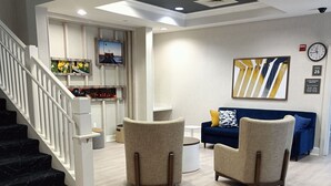 A modern living room with a staircase, two armchairs, a blue sofa, and a wall clock. - Comfort Inn & Suites Virginia Beach - Norfolk Airport (Virginia Beach)