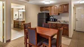 A compact kitchen with wooden cabinets, a refrigerator, and a dining area with a table and chairs. - Comfort Inn & Suites Virginia Beach - Norfolk Airport (Virginia Beach)