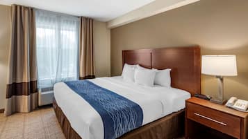 A hotel room with a bed, a bedside table with a lamp, a phone, and a window with curtains.